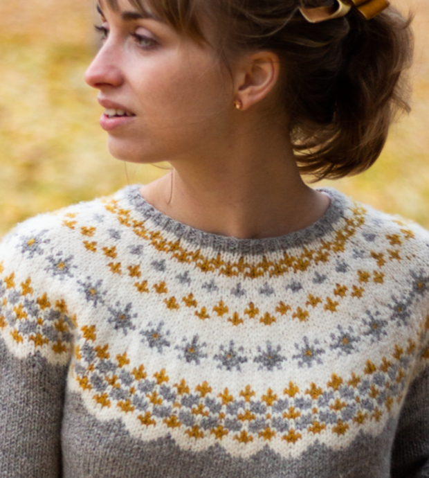 Photo of girl in Svendsdatter sweater. A grey sweater with a white yoke and gold and grey Scandinavian motifs.